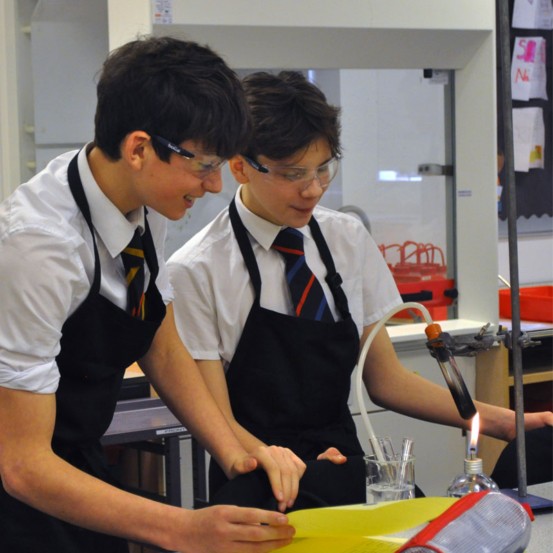 Photo of two students with bunsen burner in chemistry lab, science class